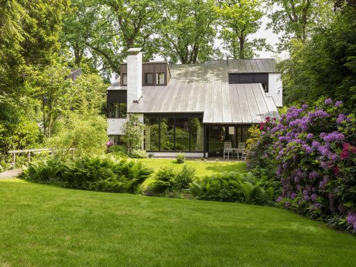 Modernes Haus mit Garten und bunten Blumen, umgeben von Bäumen.