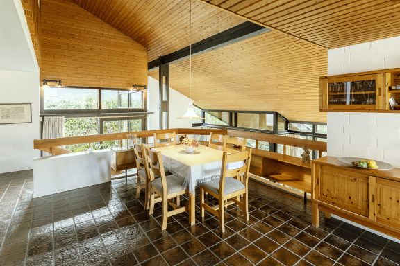 Helles Esszimmer mit Holzdetails, großem Tisch und Fenstern, die nach außen blicken.