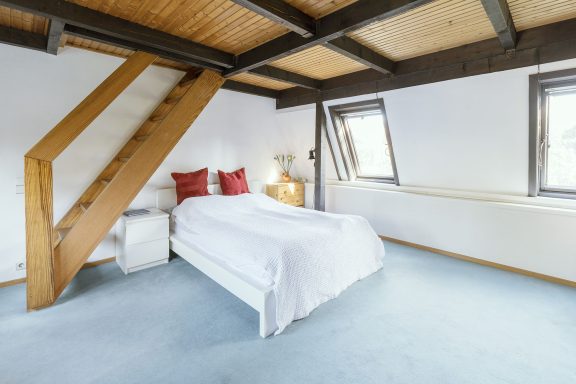 Helle Schlafzimmer mit einem Doppelbett, zwei Fenstern und Holzbalken.