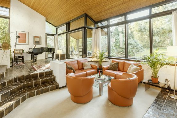 Helles Wohnzimmer mit runden orangenen Sesseln und großen Fenstern zur Natur.