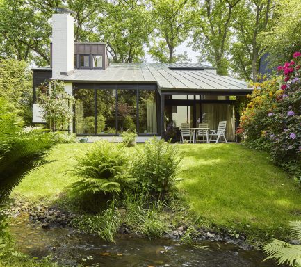 Modernes Haus mit großen Fenstern, umgeben von grüner Landschaft und bunten Blumen.