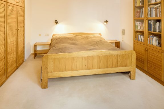 Helles Schlafzimmer mit einem Holzbett und einer Bücherregalwand.
