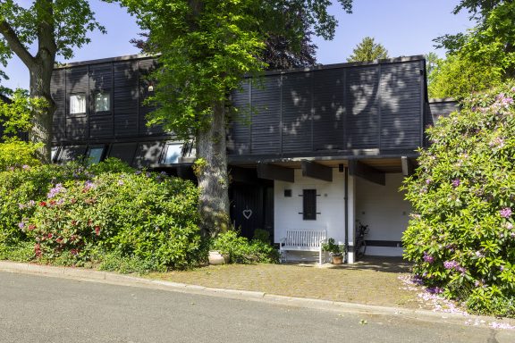 Modernes schwarzes Haus, umgeben von üppigem Grün und bunten Blumen.
